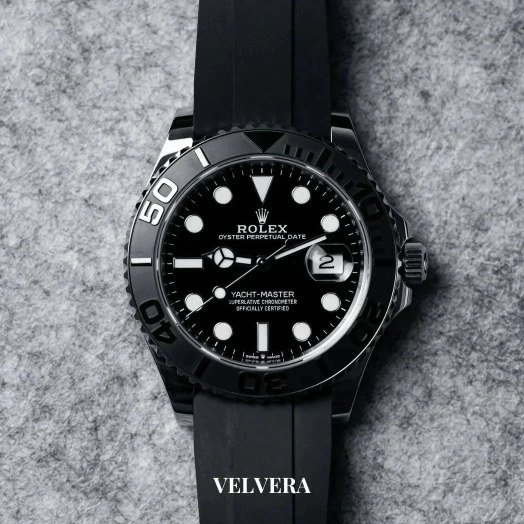 Black Rolex Yacht-Master watch with black rubber strap on grey textured background, Velvera logo