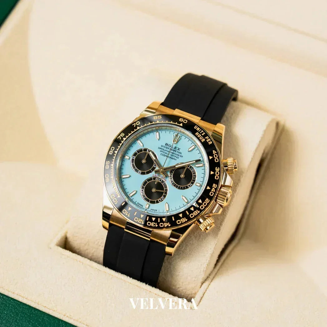 Gold Rolex Daytona watch with blue dial and black strap in cream display box, Velvera logo