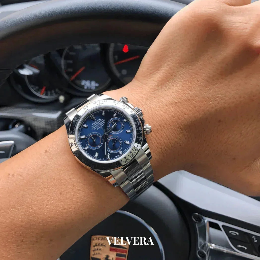 Luxury stainless steel chronograph watch with blue dial on wrist inside a Porsche car