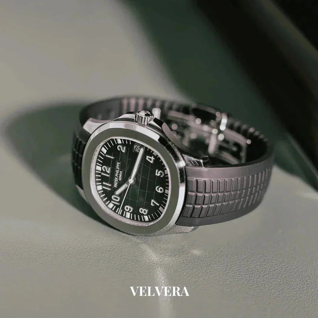 Luxury black dial stainless steel watch with rubber strap on a gray surface, Velvera branding