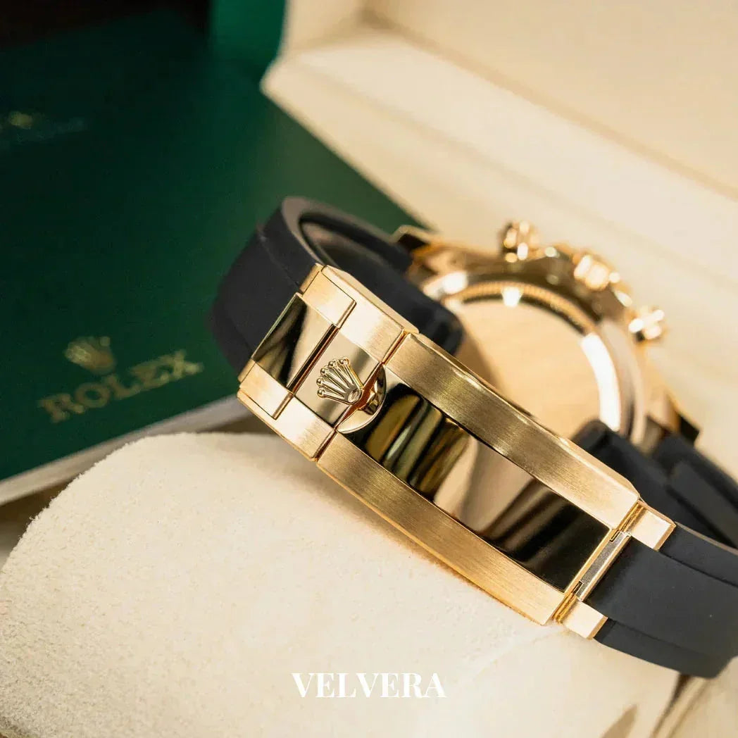 Gold Rolex watch with black strap on cushion, green Rolex box in background, Velvera branding