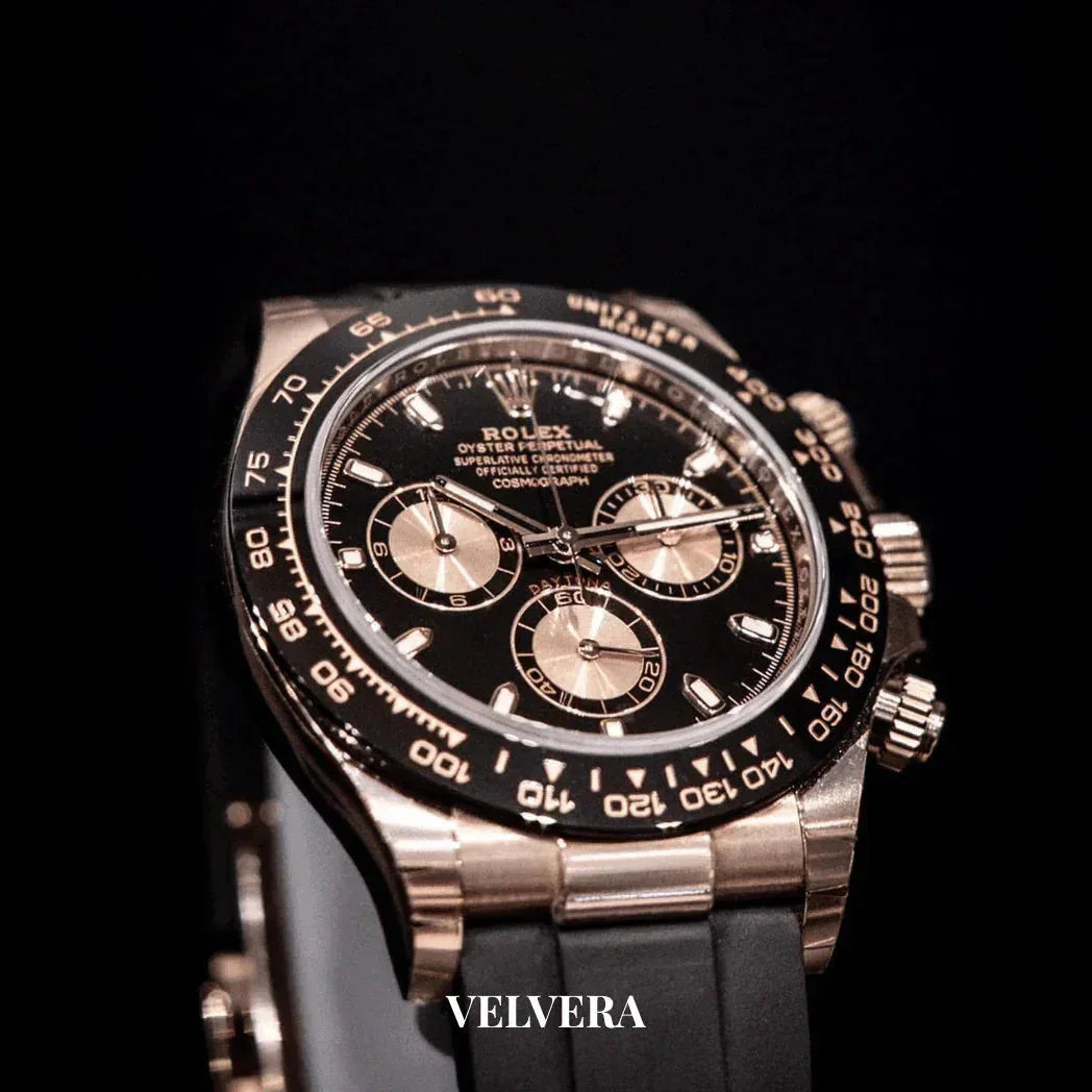 Luxury Rolex chronograph watch with black dial and gold accents on black strap, Velvera branding