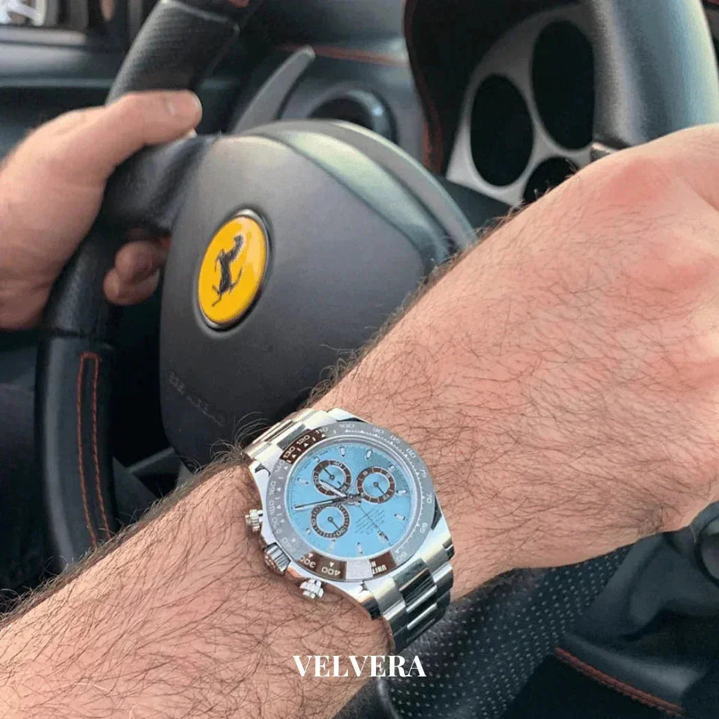 Luxury silver chronograph watch on wrist, holding Ferrari steering wheel, Velvera branding