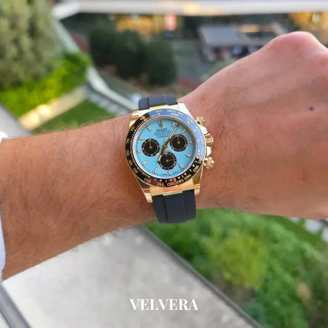 Gold and blue Rolex Daytona watch with black strap on wrist outdoors, Velvera branding