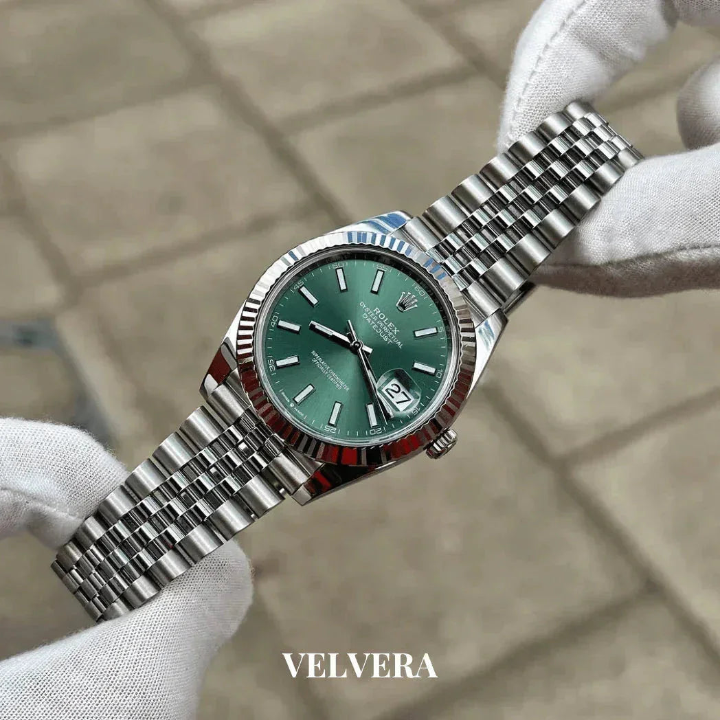 Luxury stainless steel watch with green dial and date, held by gloved hands, Velvera branding