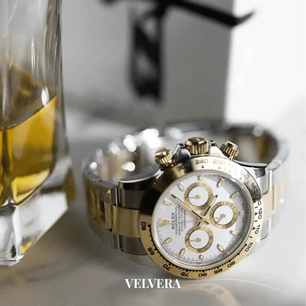 Luxury Rolex Daytona two-tone gold and silver watch beside a whiskey glass, Velvera branding
