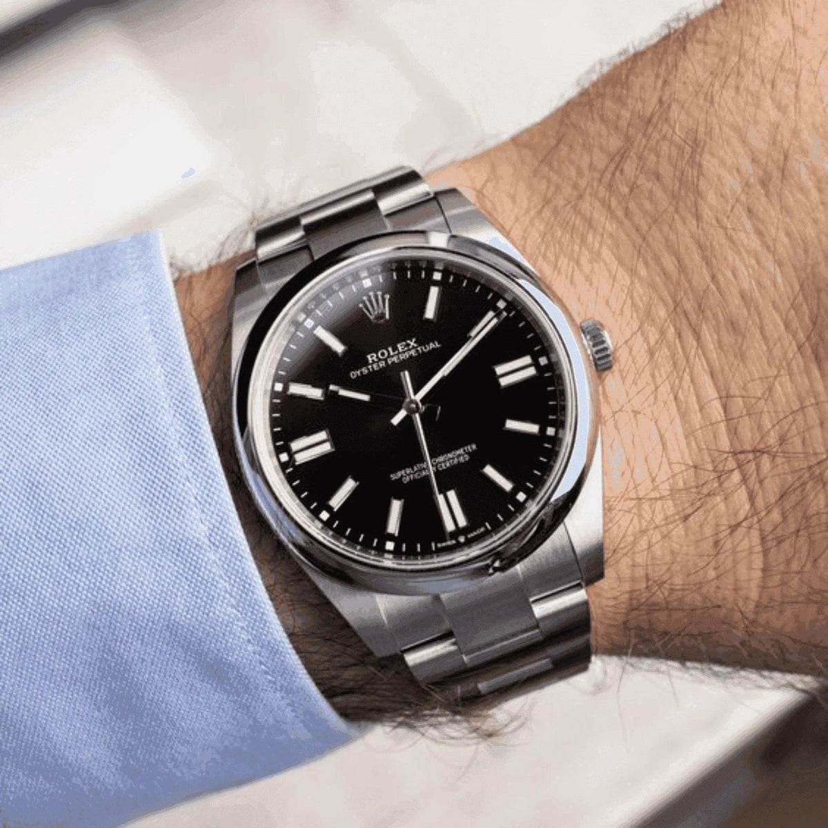 Men's classic stainless steel Rolex watch with black dial on wrist, blue shirt cuff