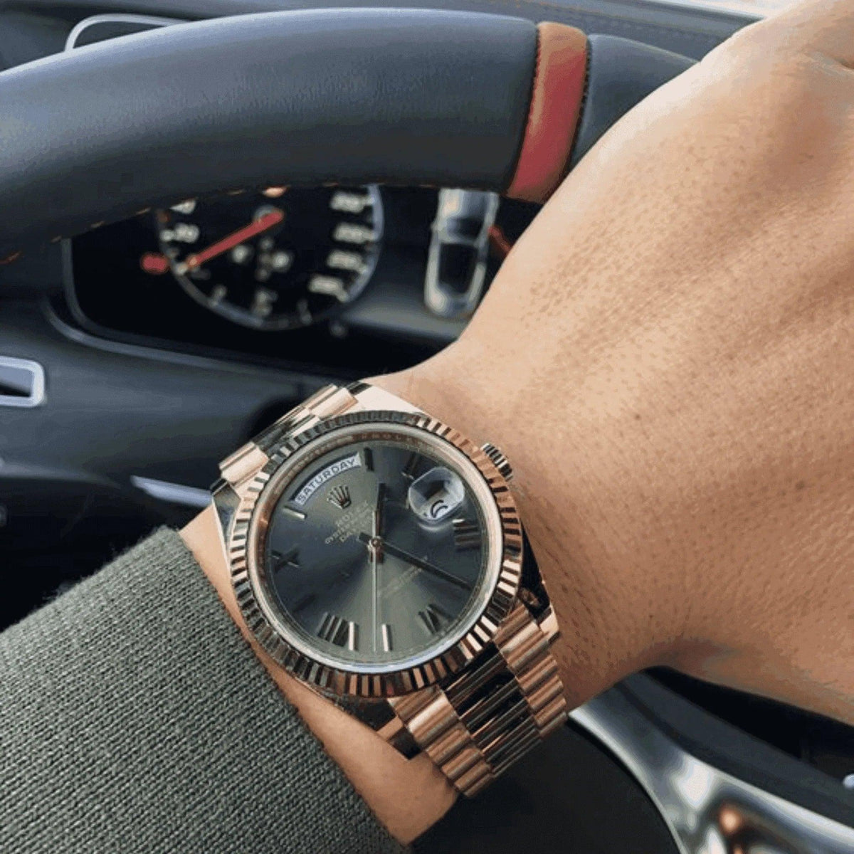 Men's Everose gold day-date watch on wrist, black dial, in luxury car interior