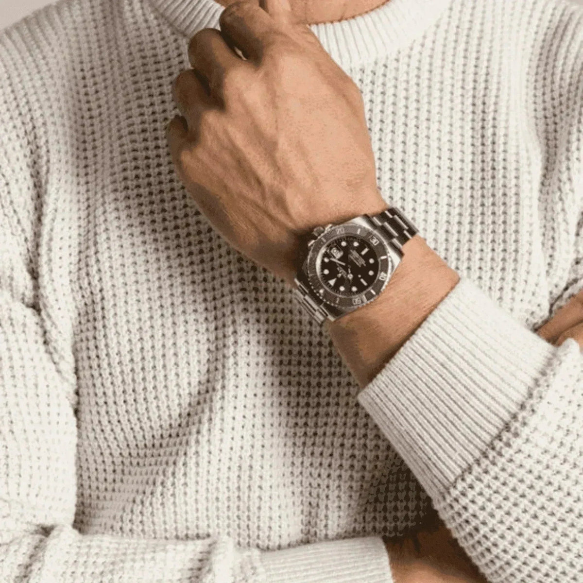Man wearing stainless steel dive watch with black bezel and white textured sweater.