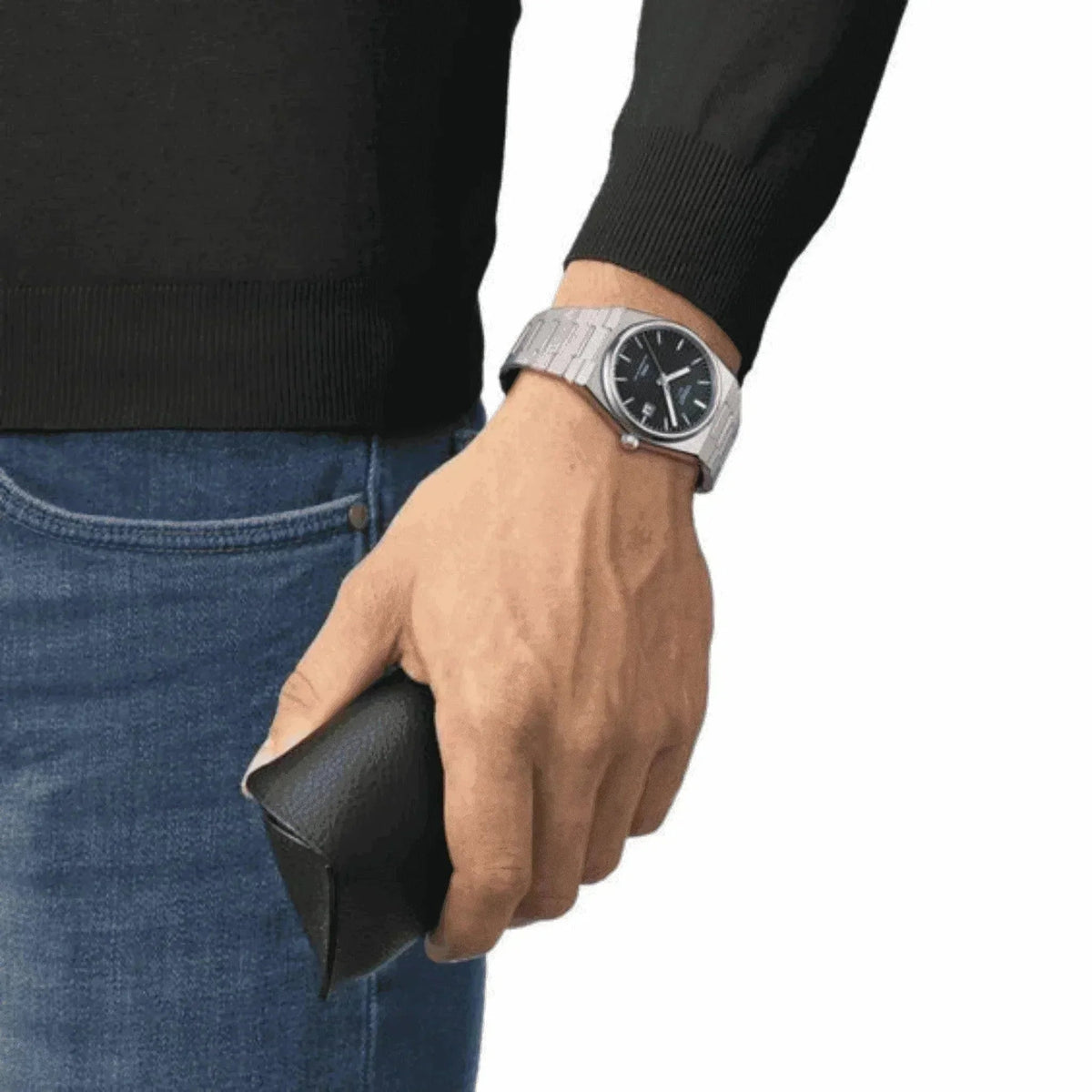 Man wearing a silver wristwatch with black dial and holding a black leather case