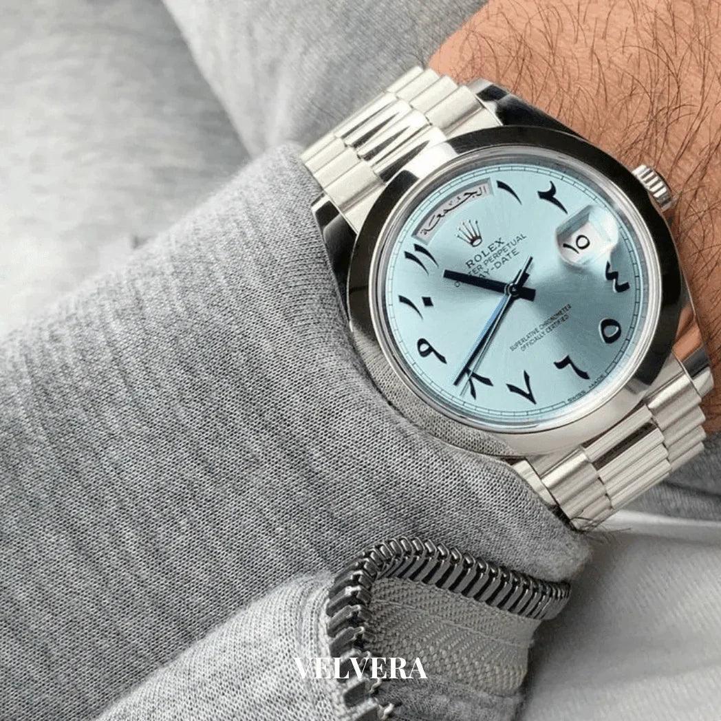 Silver Rolex watch with ice blue Arabic dial on wrist, grey sleeve, Velvera branding visible