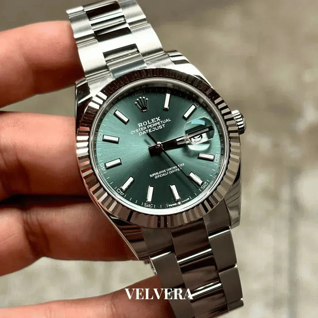 Hand holding silver Rolex Datejust watch with green dial and fluted bezel, Velvera branding