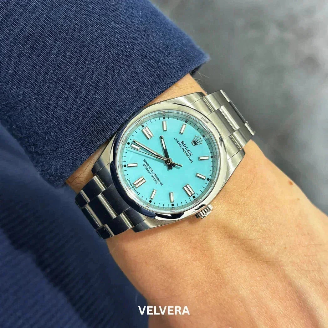 Stainless steel Rolex watch with turquoise dial on wrist, blue sleeve visible