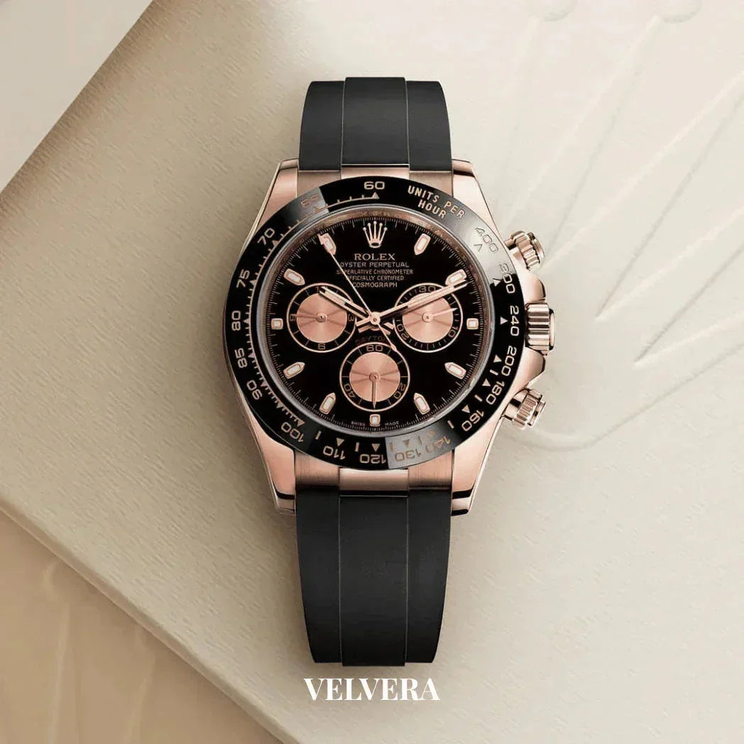 Luxury Rolex black and gold chronograph watch on black strap, displayed on light surface, Velvera branding