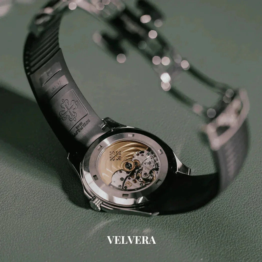 Luxury automatic watch caseback with exposed movement and black band on green surface, Velvera logo