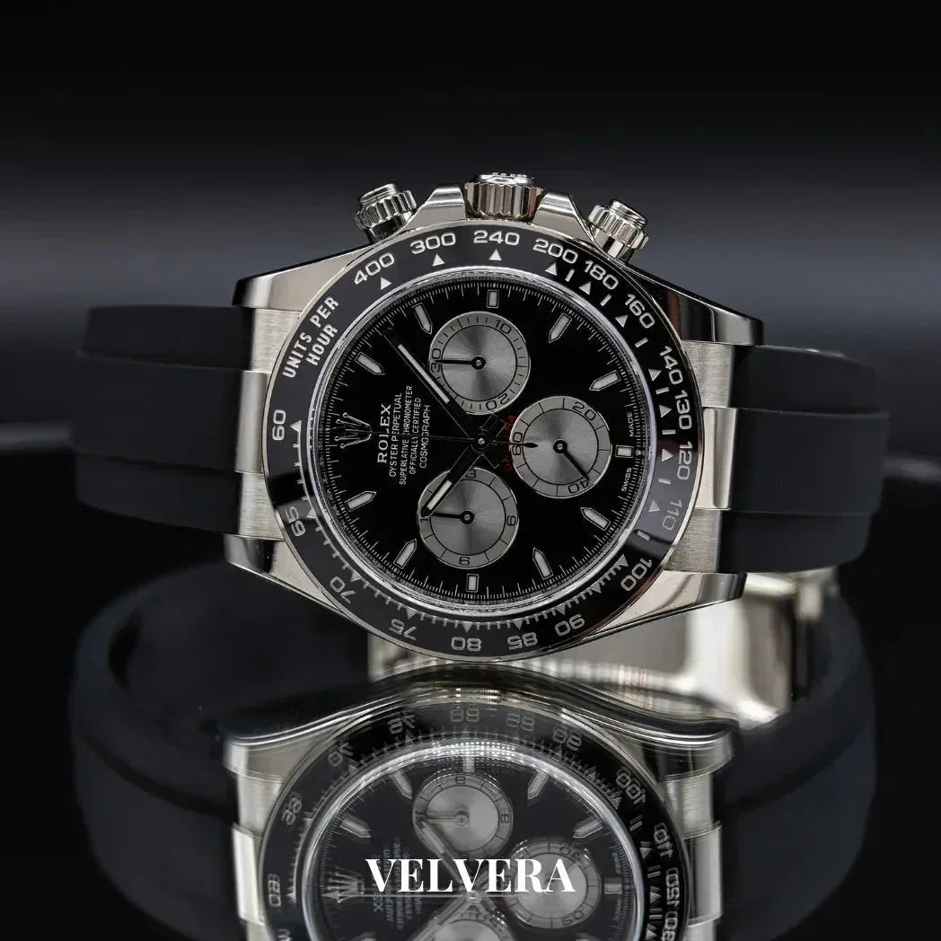 Luxury Rolex black chronograph watch with black rubber strap on reflective surface, Velvera branding