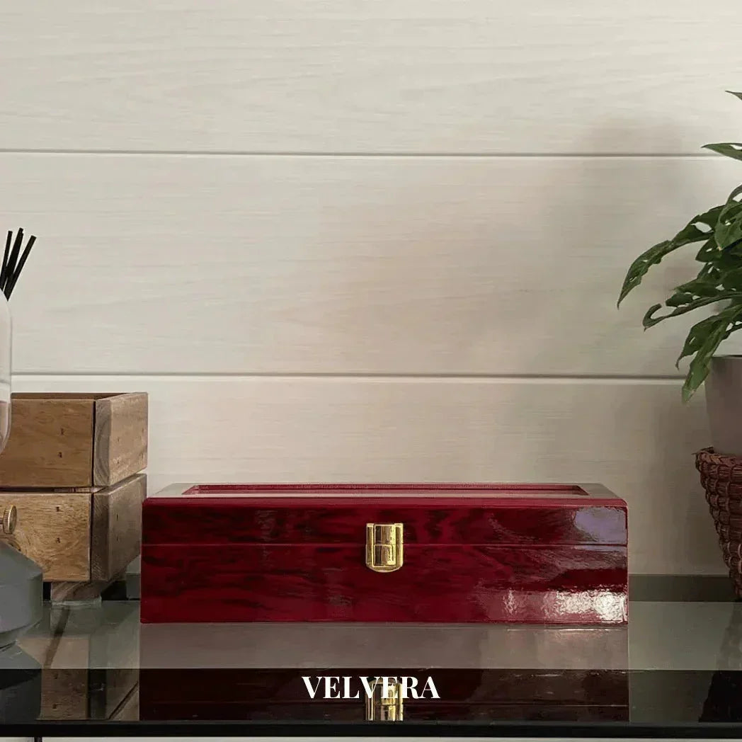 Glossy red wooden jewelry box with gold clasp on glass table, plant and wooden blocks nearby, Velvera