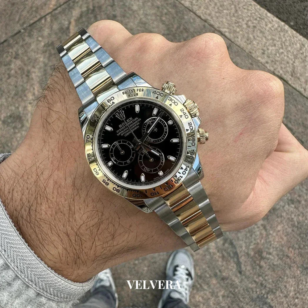 Two-tone Rolex Daytona watch with black dial on wrist, outdoor stone background, Velvera branding