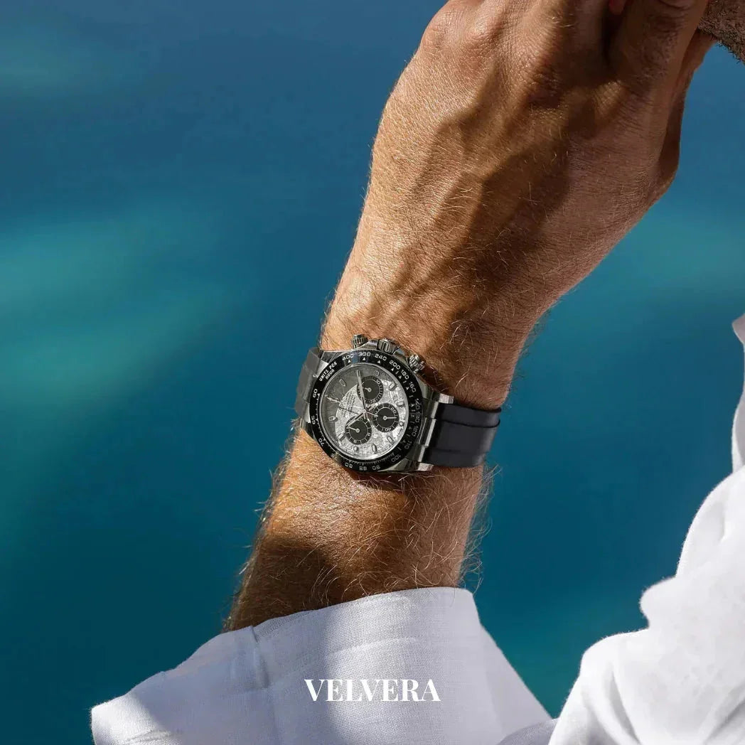 Luxury black chronograph watch on wrist, white shirt, VELVERA logo, blue background
