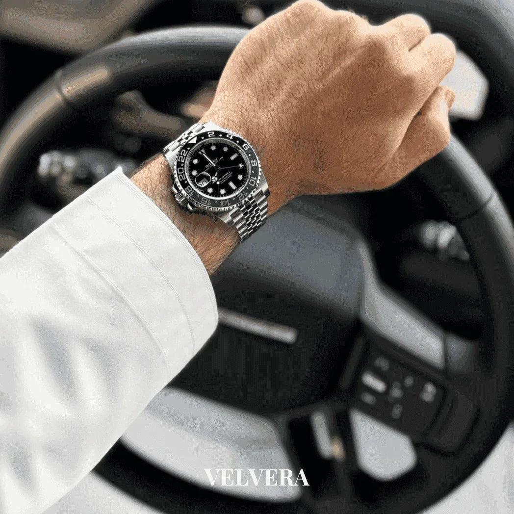 Luxury silver wristwatch on man's hand at steering wheel, VELVERA branding visible