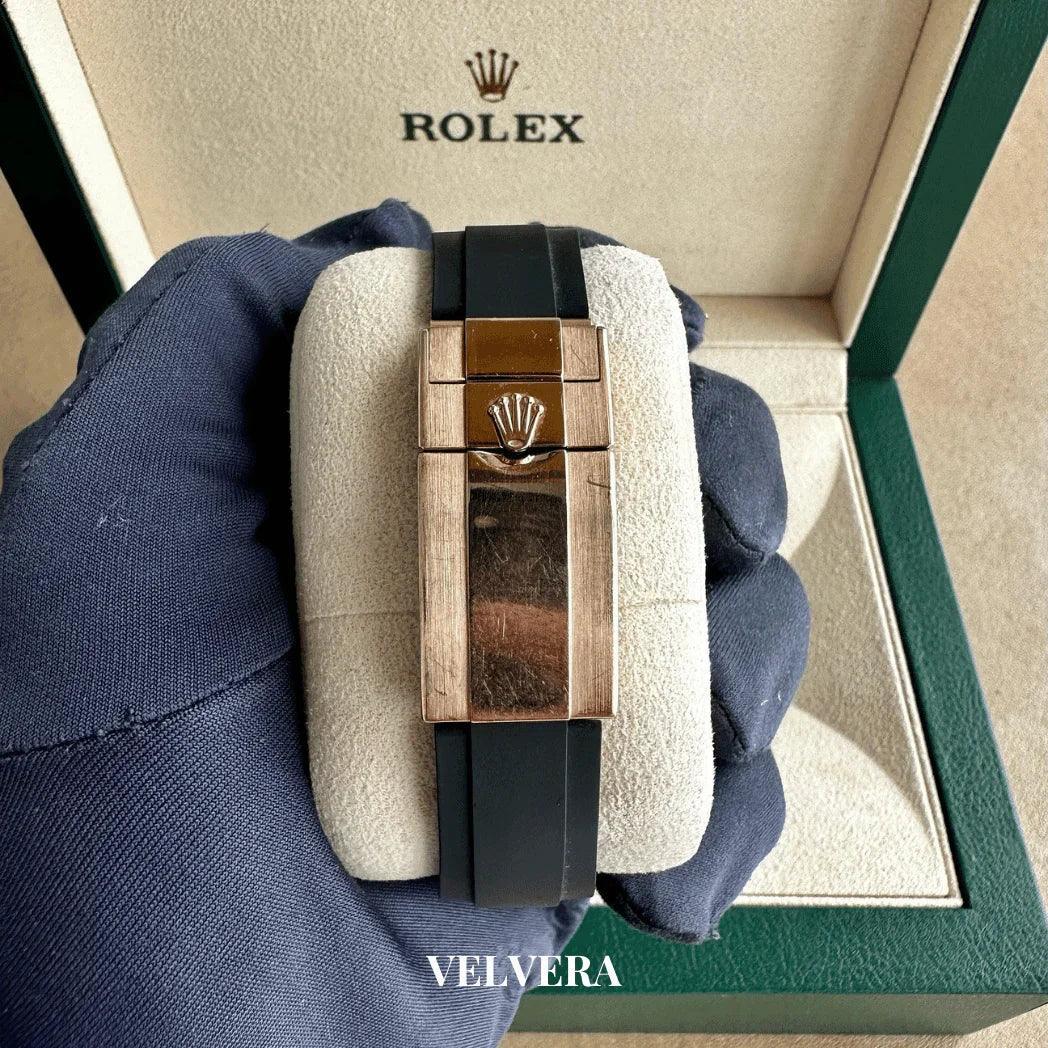 Rolex watch with black strap and gold clasp held in gloved hand, luxury green box background