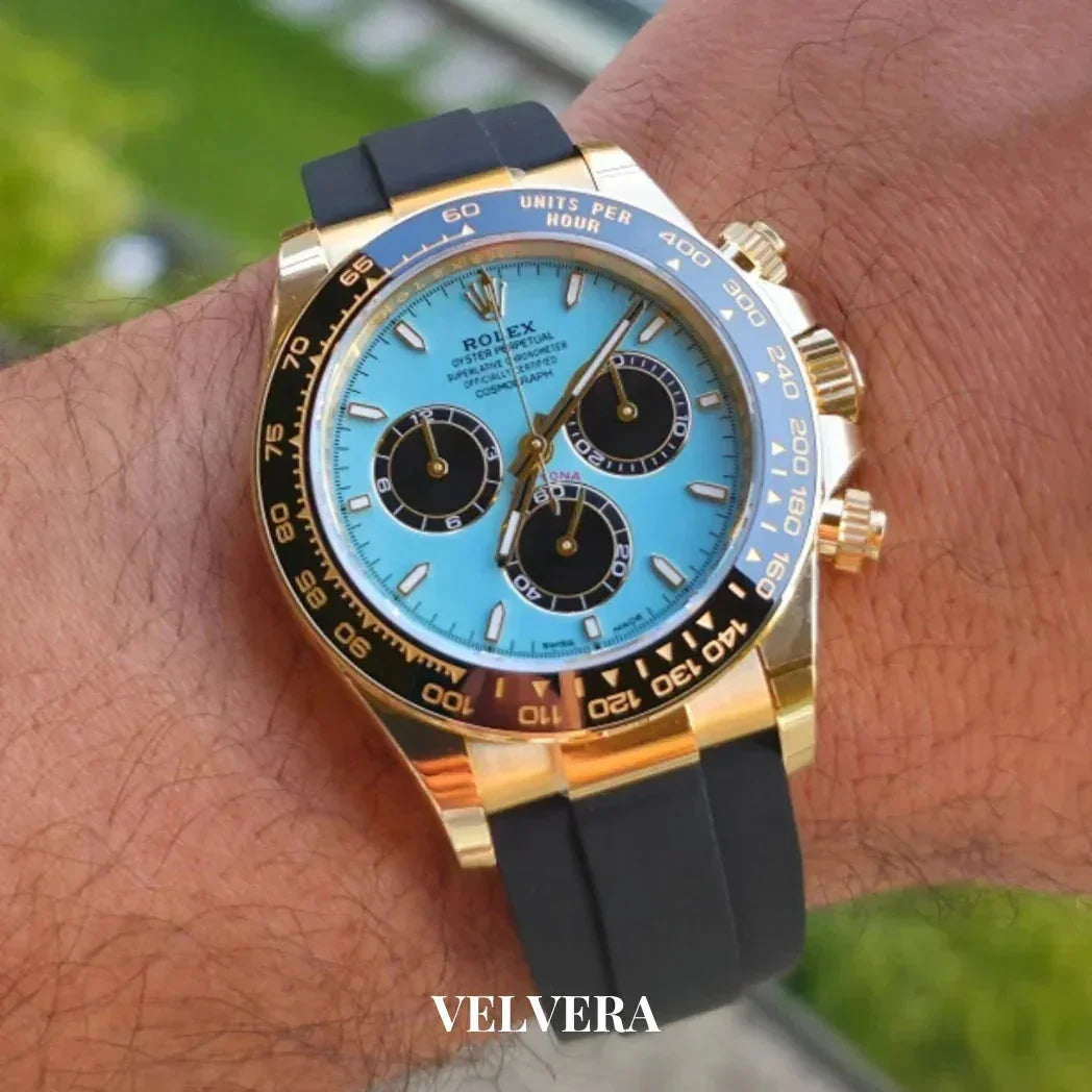 Rolex Daytona gold watch with turquoise dial and black strap on wrist outdoors