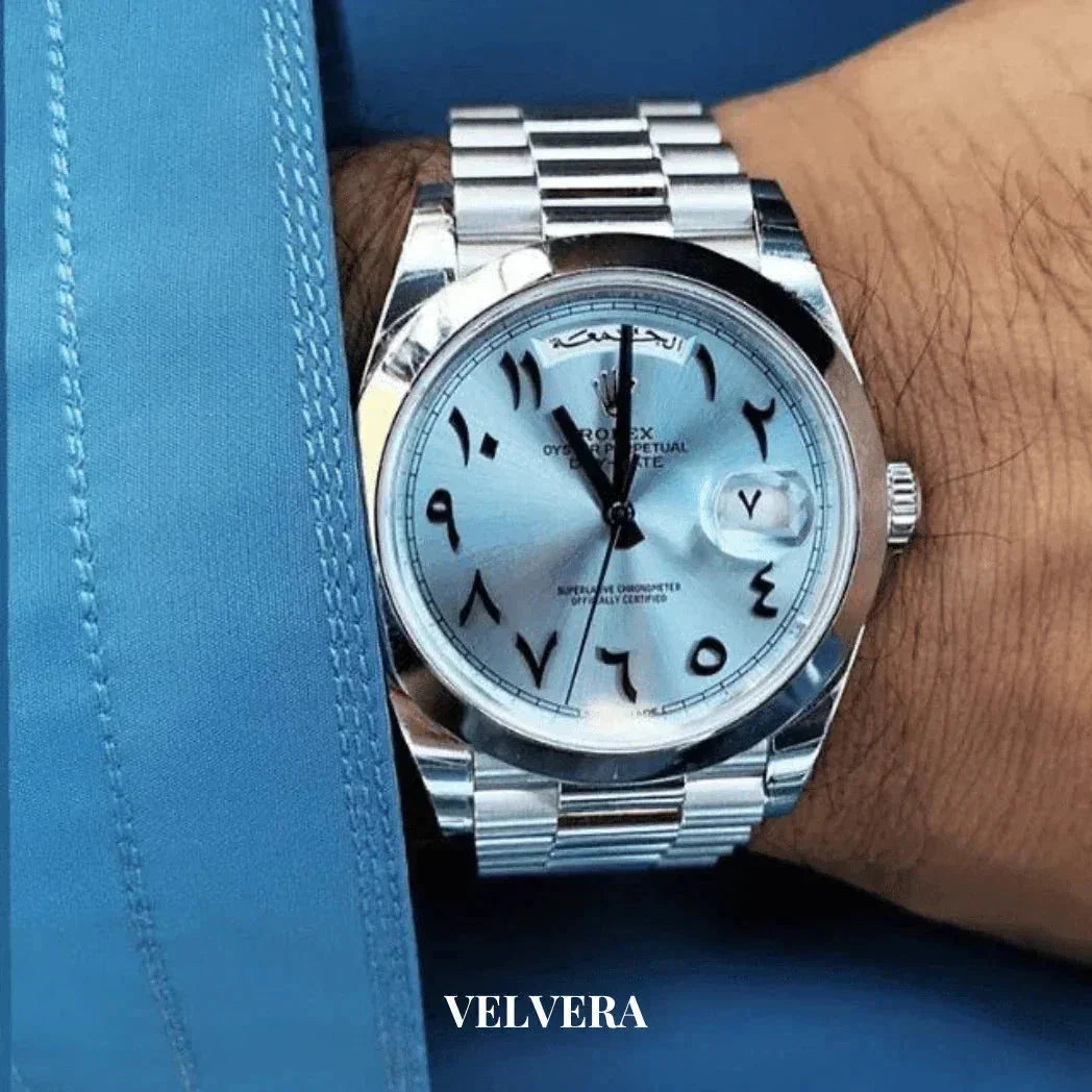Luxury Rolex wristwatch with Arabic numerals, silver band, worn on wrist, blue shirt, Velvera