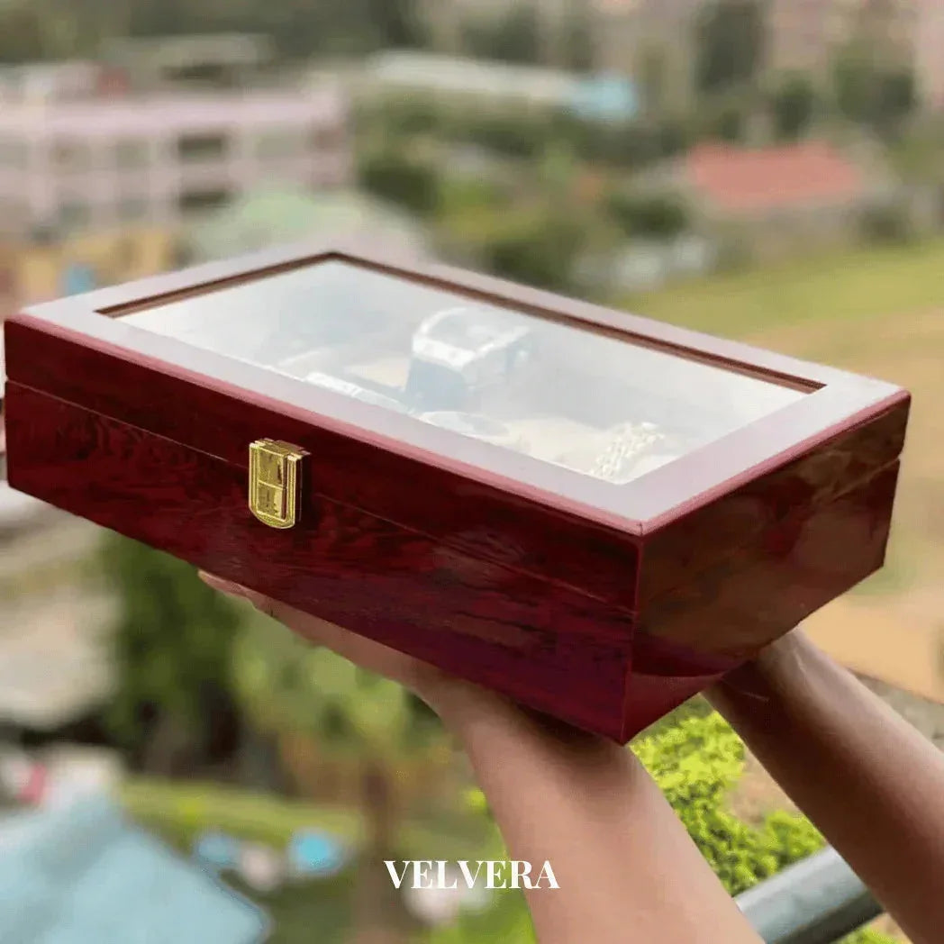 Wooden watch box with glass lid and gold latch held outdoors, VELVERA branding visible