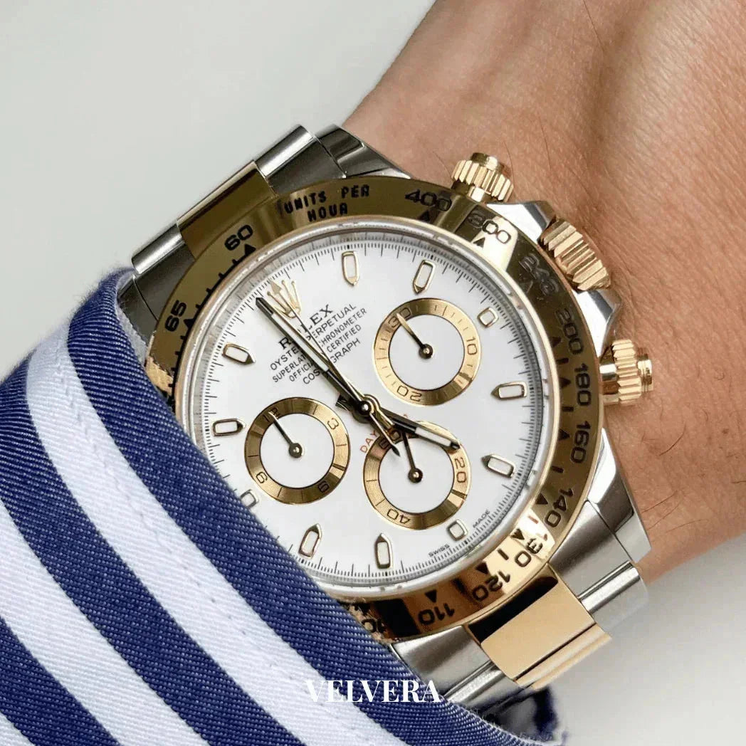 Gold and silver chronograph luxury watch with white dial on wrist, blue striped shirt visible