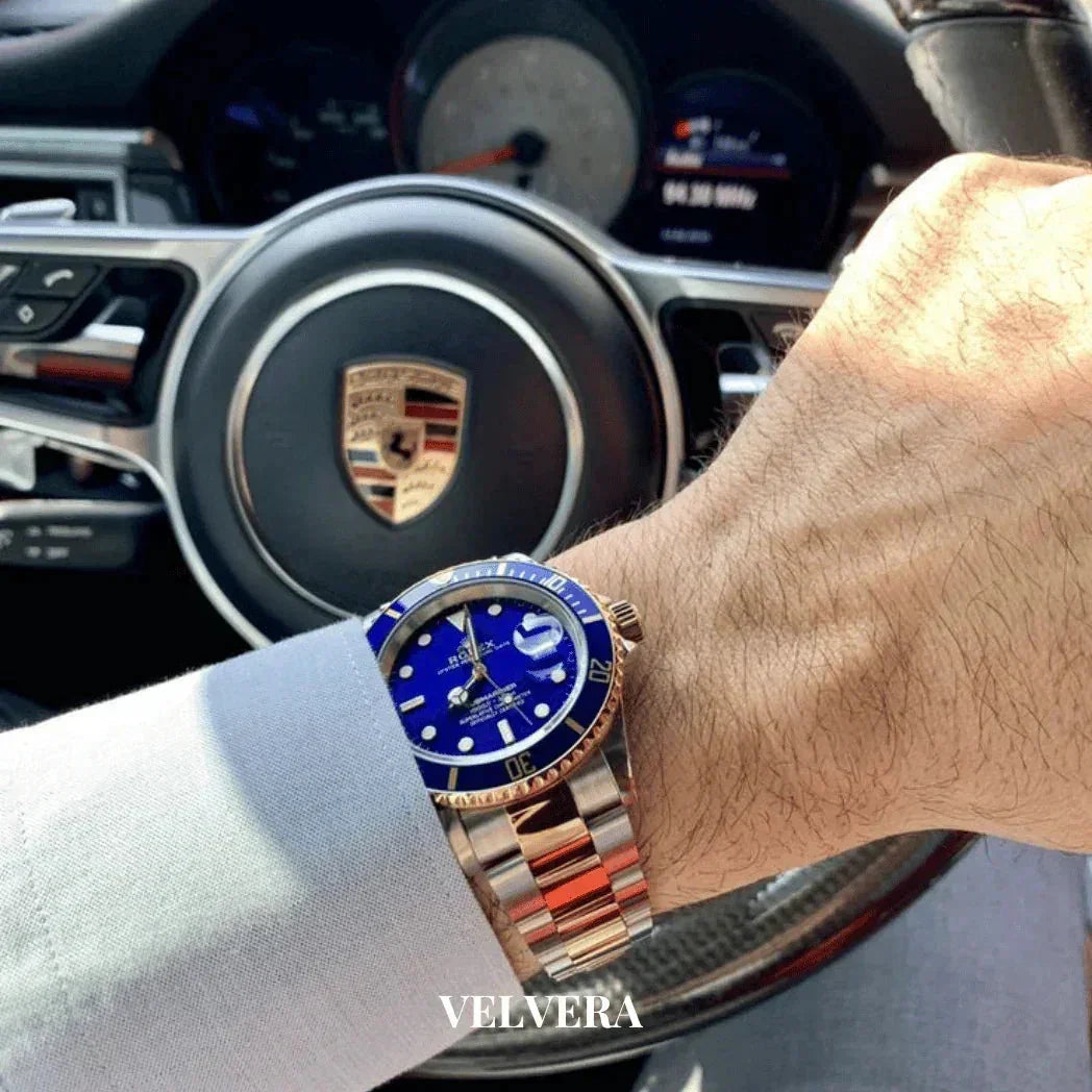 Luxury blue dial wristwatch on wrist inside a Porsche car, VELVERA branding visible.