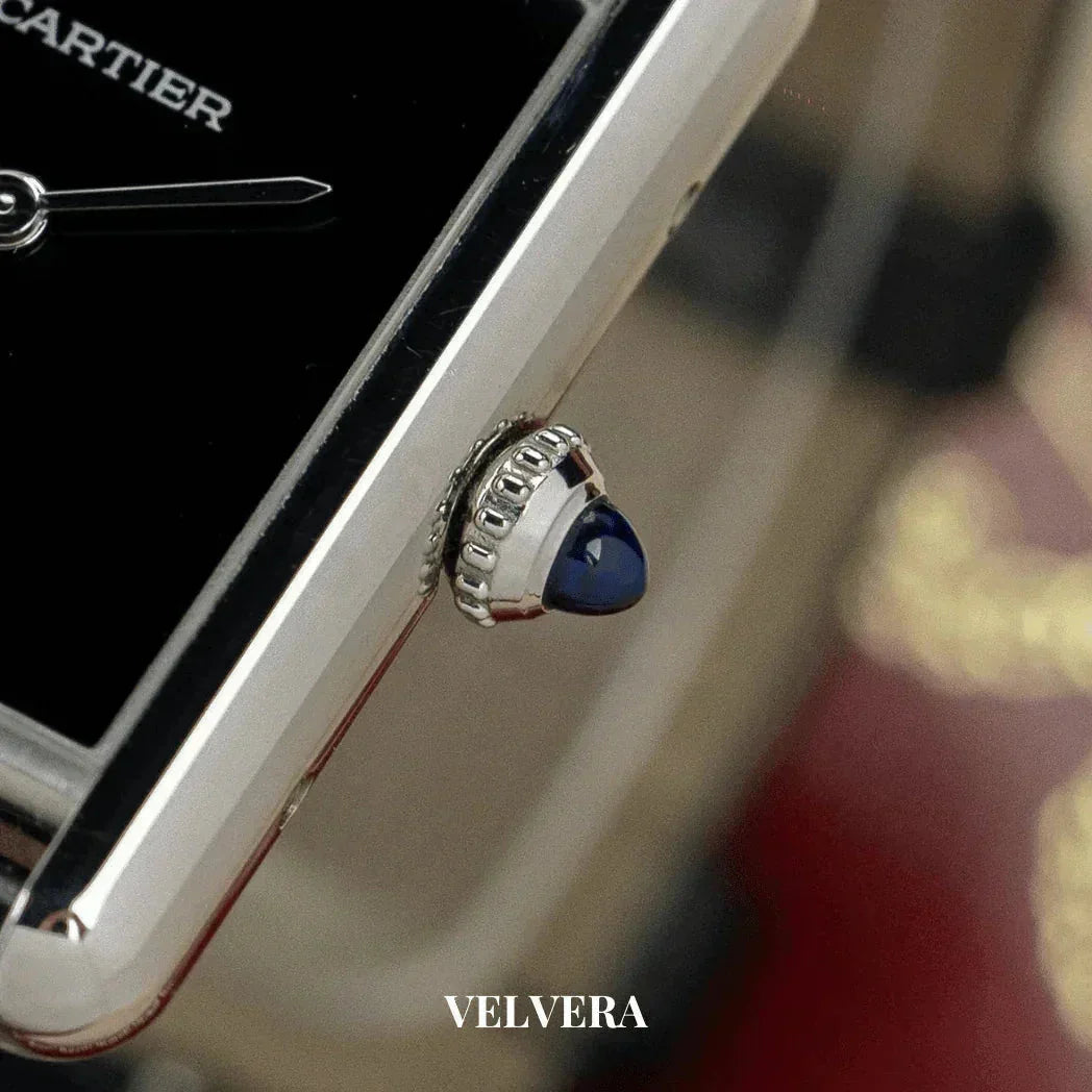 Close-up of a Cartier watch crown with blue cabochon, black dial, and Velvera logo