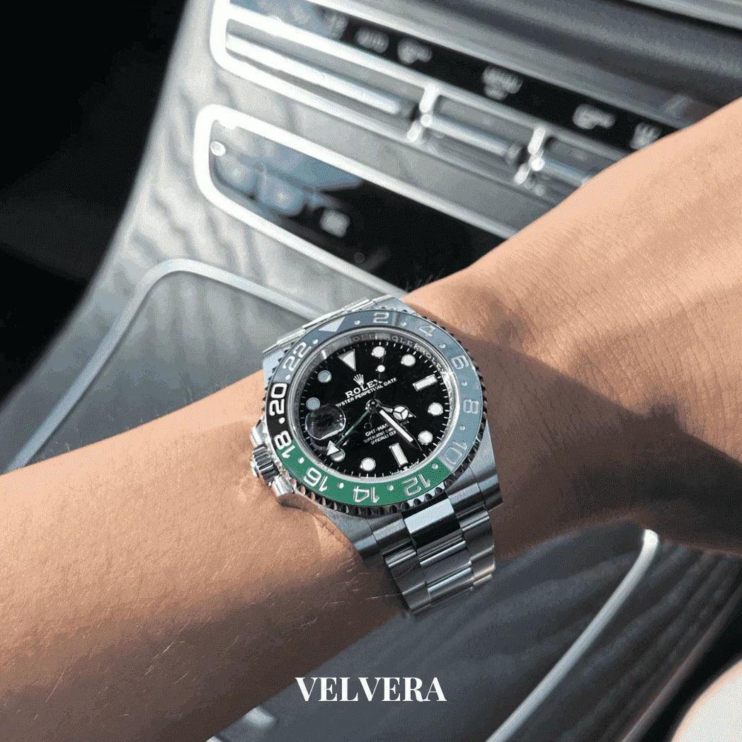 Luxury Rolex watch with black dial and green bezel on wrist in car, VELVERA branding visible