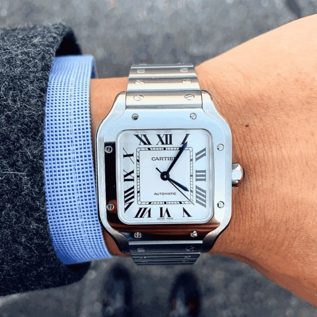 Cartier Santos men's silver watch with Roman numerals on wrist, elegant outfit visible