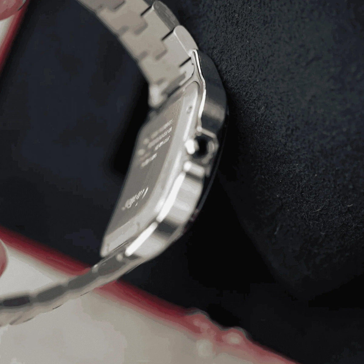 Side view of Cartier Santos men's stainless steel watch on black cushion, red box edge visible.