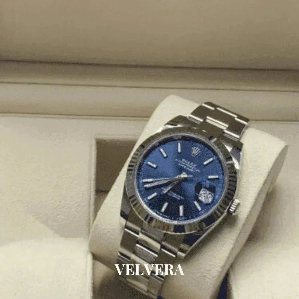 Luxury men's blue dial date watch with silver metal band on cream display, Velvera branding