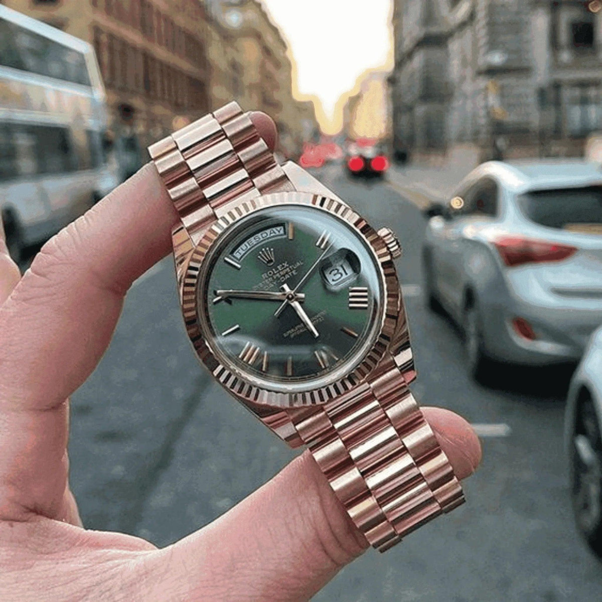 Men’s Everose gold day-date watch with green dial held in hand on city street