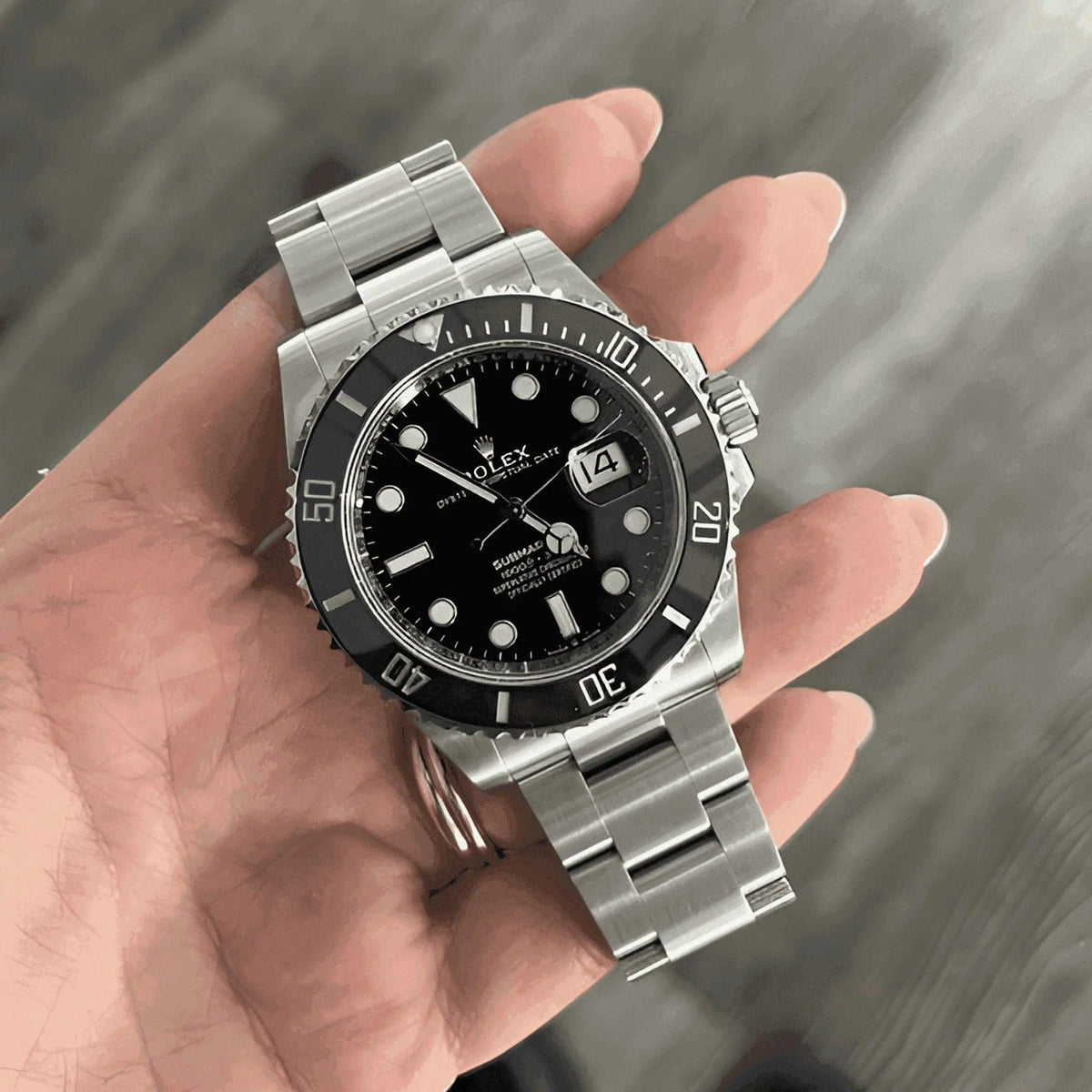 Hand holding a black dial stainless steel men's Submariner watch with date window
