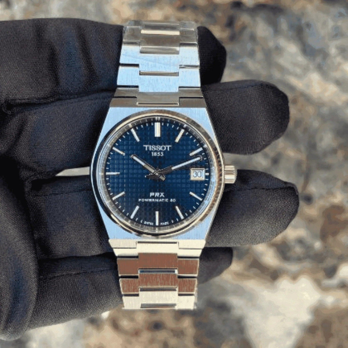 Tissot PRX Powermatic 80 men's watch with blue dial and stainless steel bracelet held by gloved hand